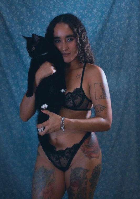 Woman in black embroidery lingerie holding a black cat against a blue patterned background